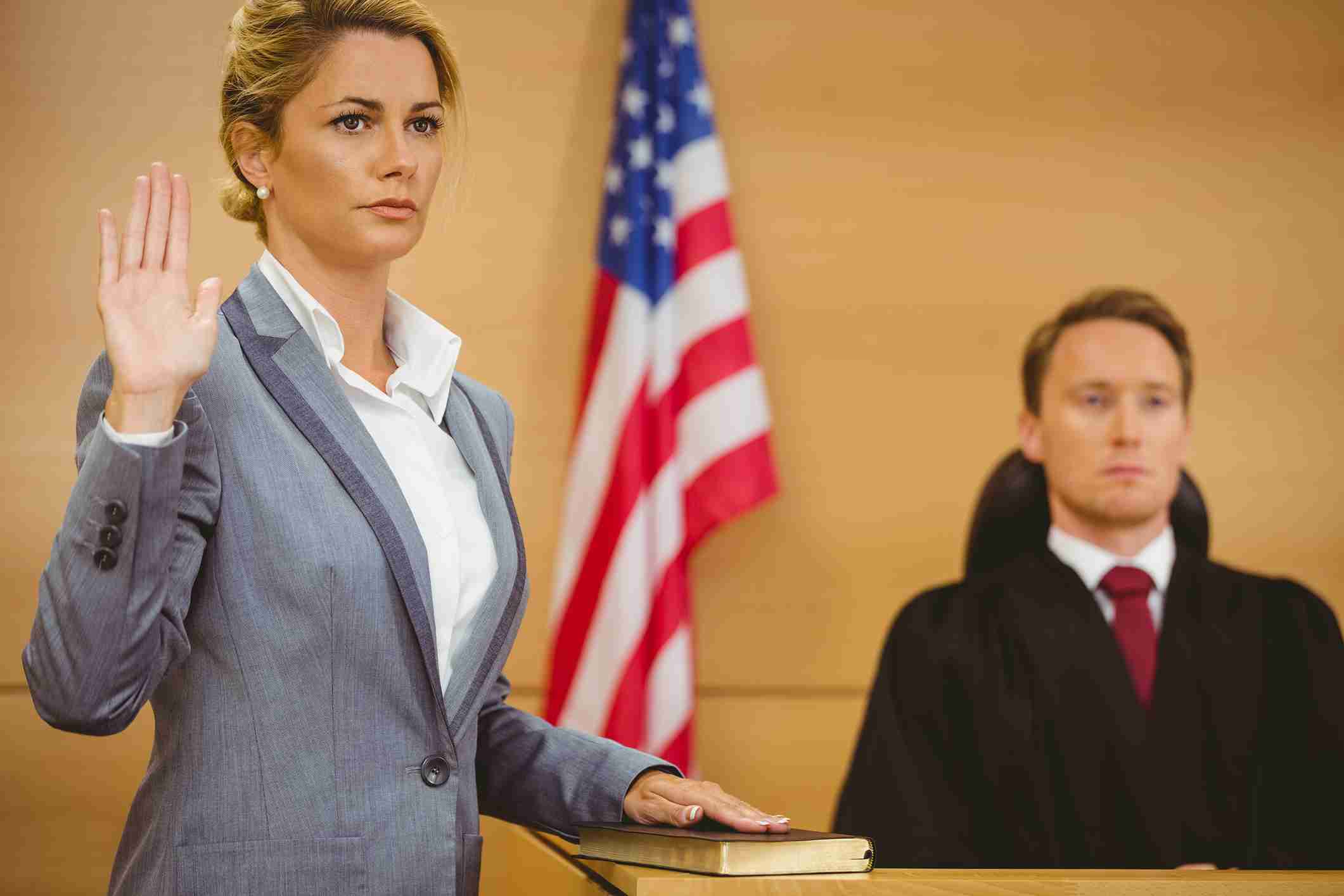 A woman taking an oath in a courtroom with a judge present.
