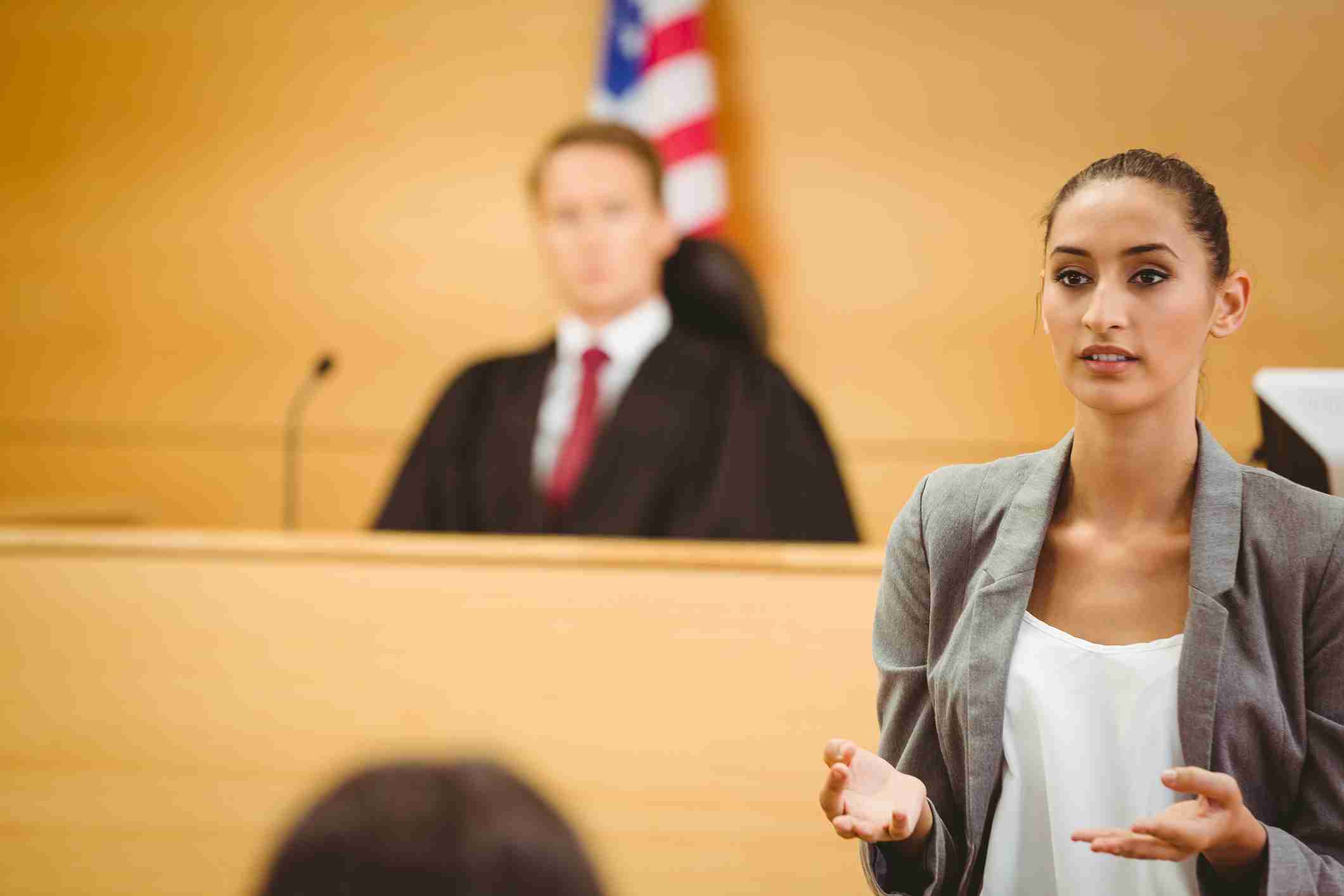 A woman speaks in court with a judge in the background.