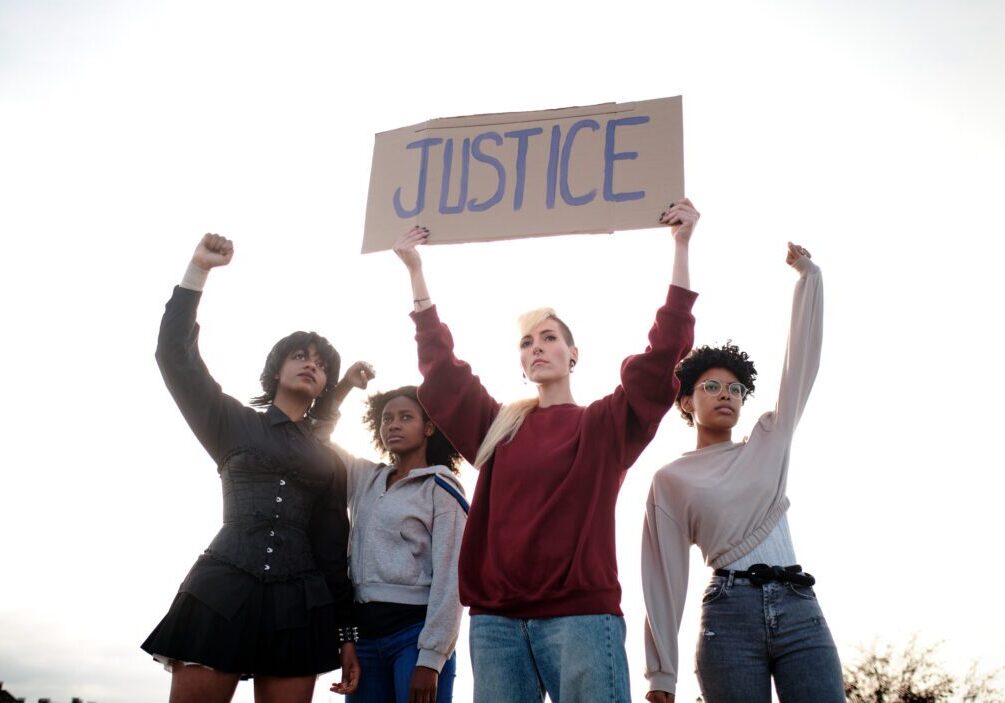 Diverse group raising fists, holding a sign saying 'JUSTICE'.