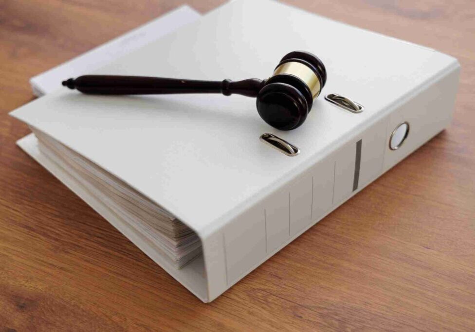 A judge's gavel resting on a thick legal binder with bullets nearby.